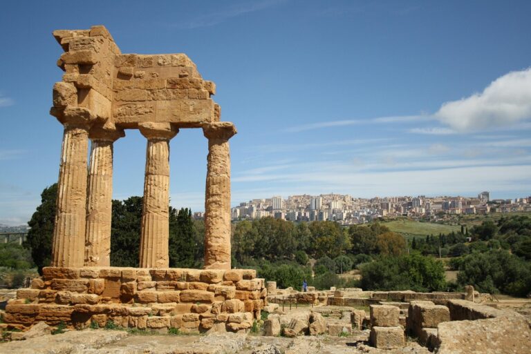Panorama delle antiche rovine della Valle dei Templi in Sicilia, con cielo blu e vegetazione circostante.