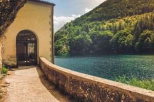Lago di Vico circondato da alberi, con cielo azzurro e monti sullo sfondo, richiamando la leggenda di Ercole.