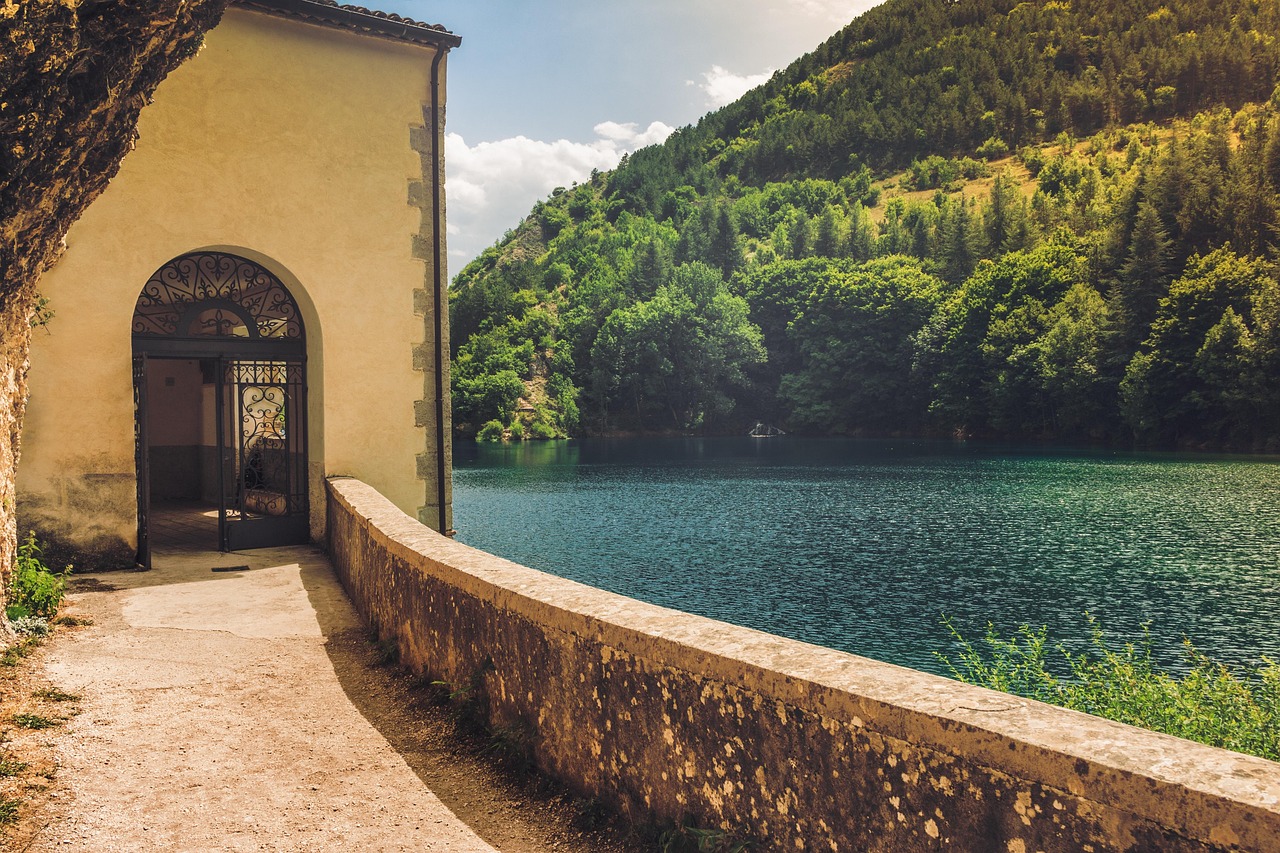 Lago di Vico circondato da alberi, con cielo azzurro e monti sullo sfondo, richiamando la leggenda di Ercole.
